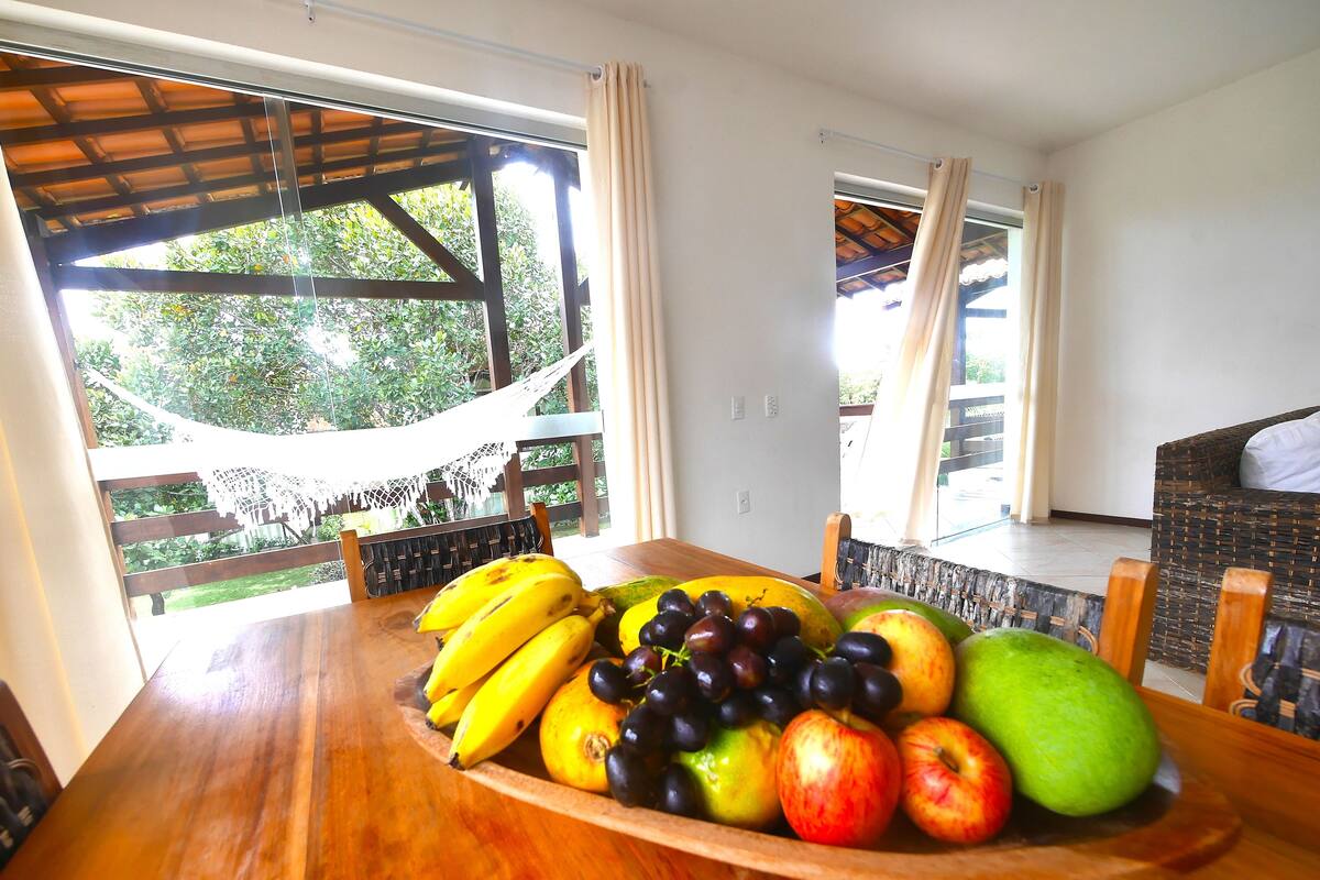 A dining table with a fruit bowl containing bananas, grapes, apples, and a mango.