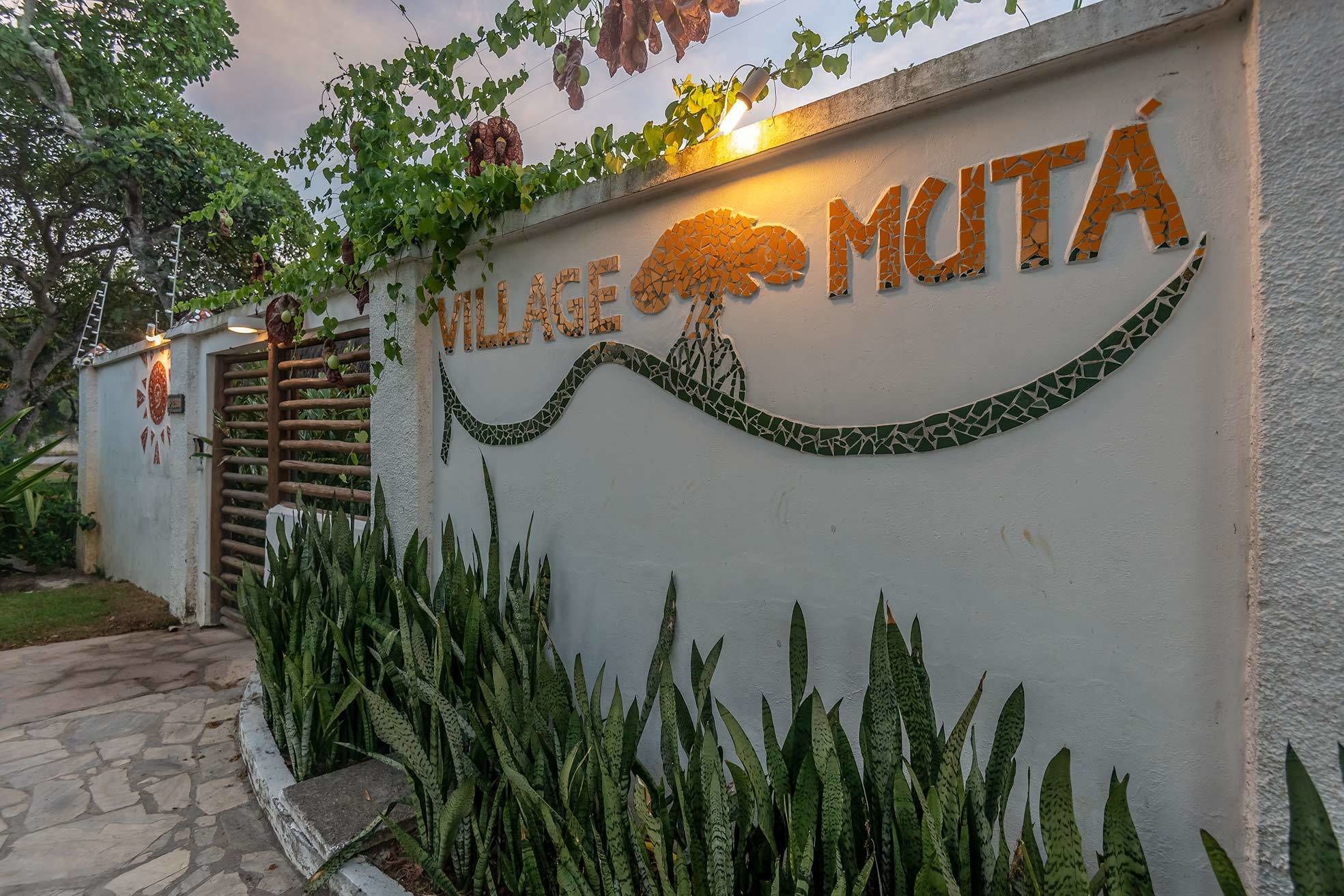 A sign with the name "VILLAGE MUTÁ" and a decorative tree design.