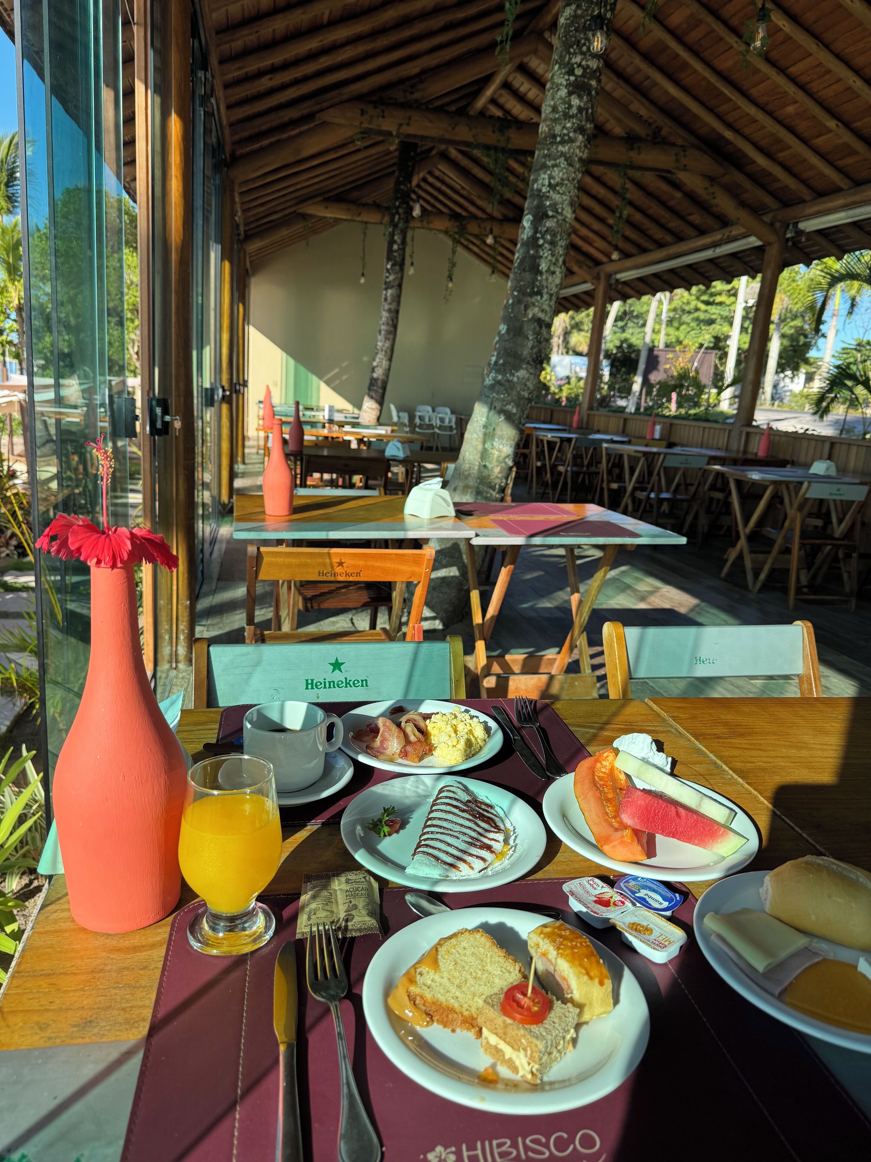 A dining table with a variety of breakfast items, including eggs, toast, and fruit, in a restaurant with a tropical setting.