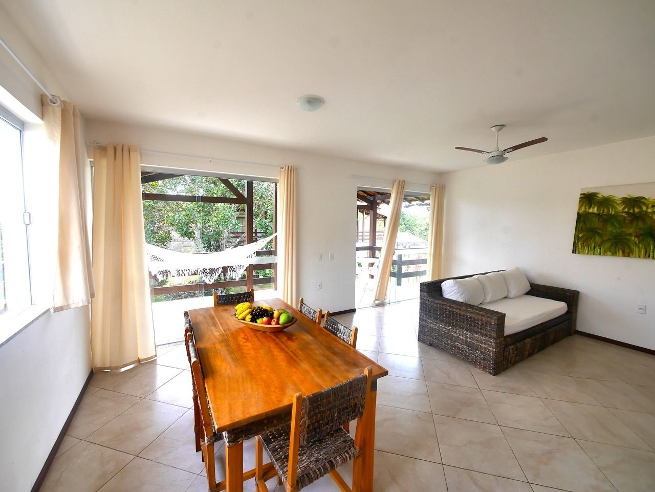 A spacious room with a wooden dining table, a wicker sofa, and a ceiling fan.