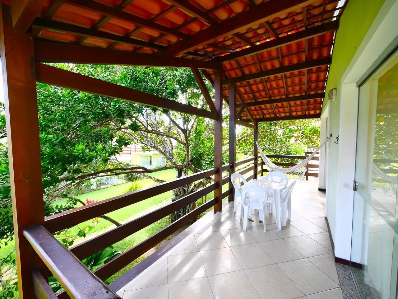 A covered patio with a wooden railing, white plastic chairs, and a table.
