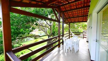 A covered patio with a wooden railing, white plastic chairs, and a table.