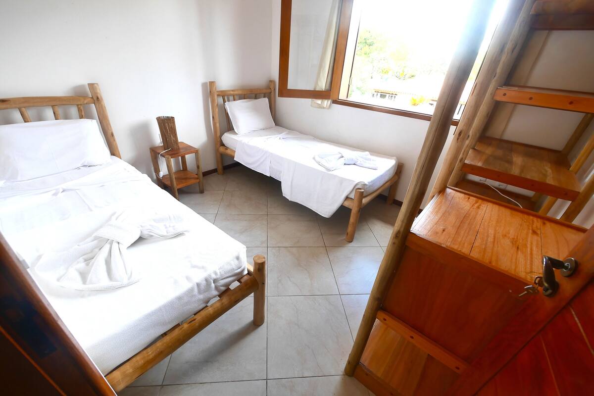 A small, wooden room with two beds, a wooden chair, and a window.