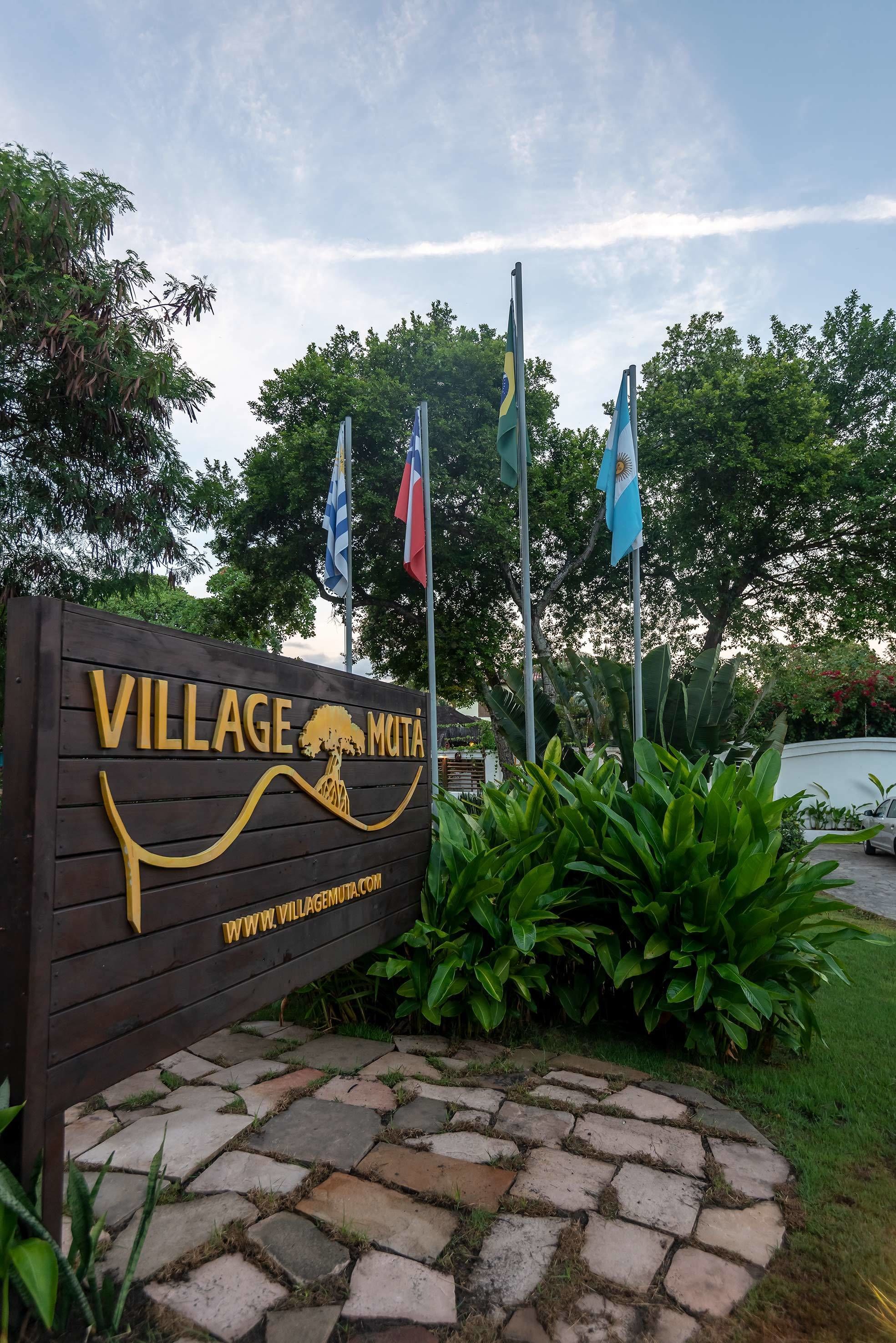 Señal de Village Muta con una dirección web y un logo que muestra un árbol y un puente.