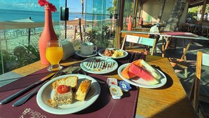 A dining table with breakfast items, a view of the beach, and a tropical setting. - Village Mutà (Porto Seguro)