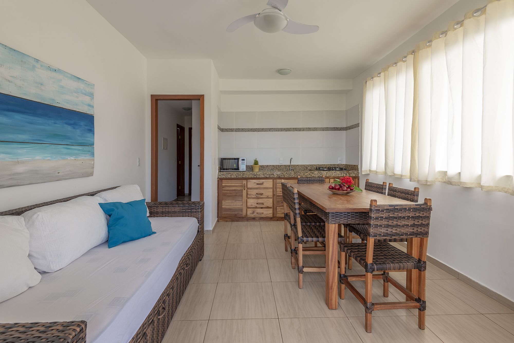 A room with a bed, a dining table with chairs, a kitchen area, and a ceiling fan.