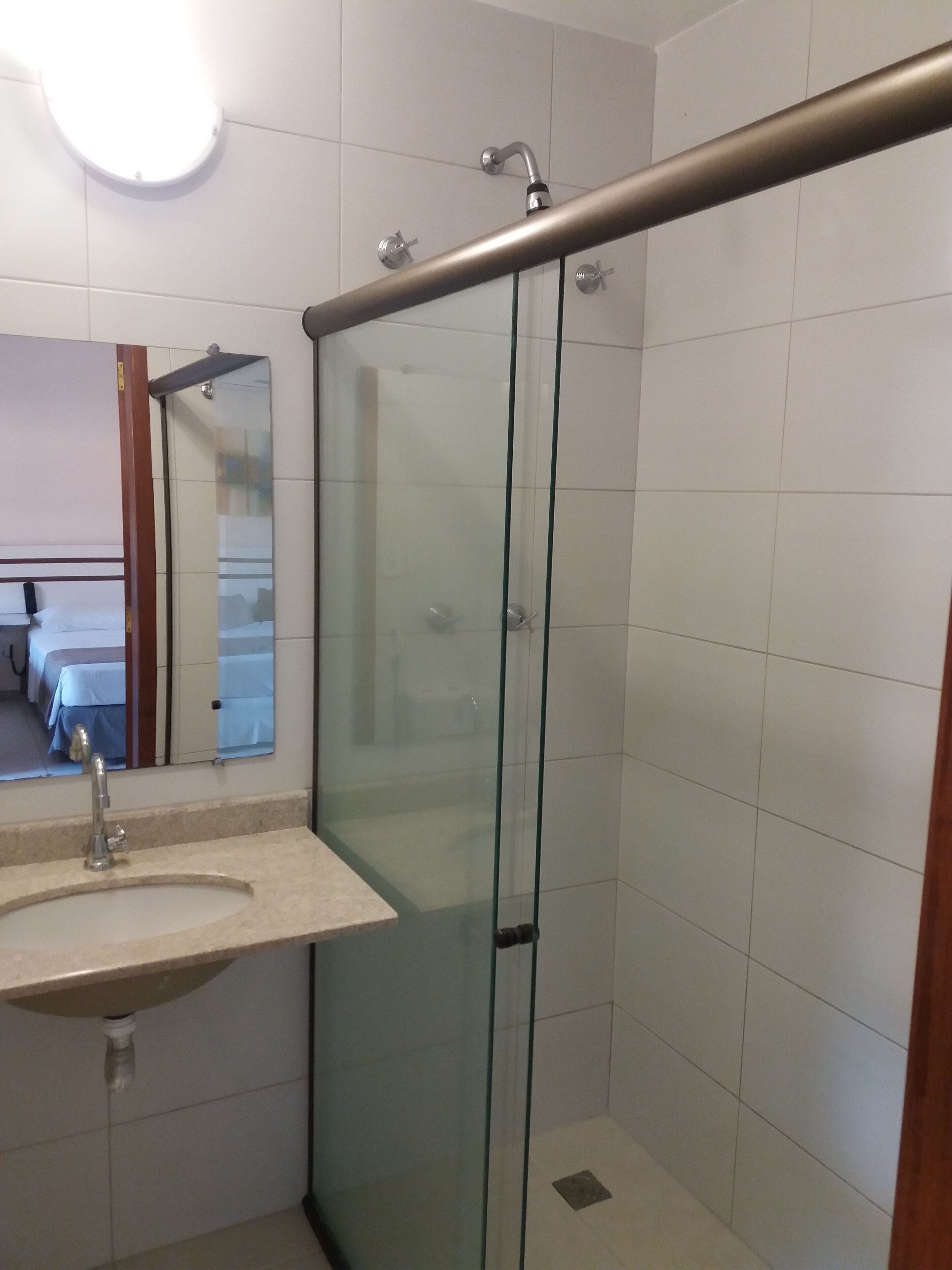 A modern bathroom with a glass shower enclosure, a sink with a mirror, and a visible showerhead.