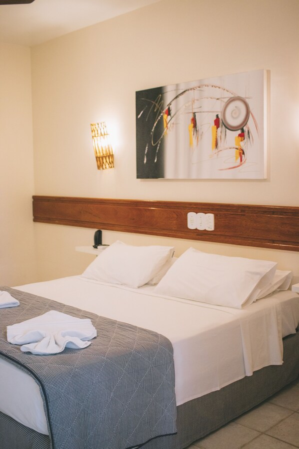 A hotel room with a neatly made bed, a wall-mounted artwork, and a wall-mounted light fixture.