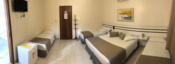 Quarto de hotel com duas camas de solteiro, uma cama de casal, uma TV fixada na parede, uma porta com uma placa e um pequeno frigorífico.