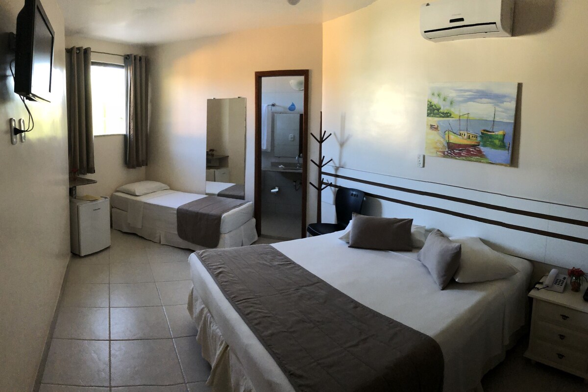 A hotel room with a bed, a desk, a chair, a television, a painting, and a bathroom.