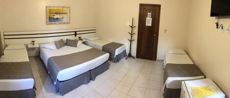 A hotel room with a large bed, two smaller beds, a desk, and a TV.