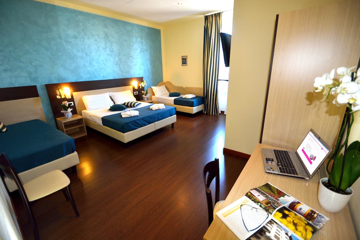 Habitación de hotel con dos camas, un escritorio con una computadora portátil, una silla, una mesita y una planta en maceta.