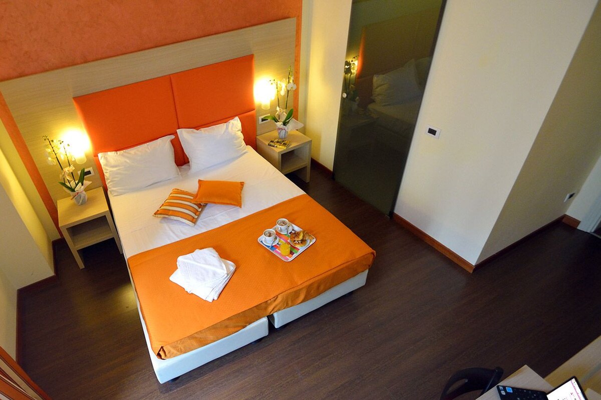 A hotel room with a bed, a nightstand, a tray with breakfast items, and a sliding door.