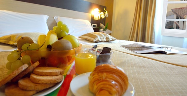 Desayuno con uvas, kiwi, croissant y jugo de naranja sobre una cama de hotel.