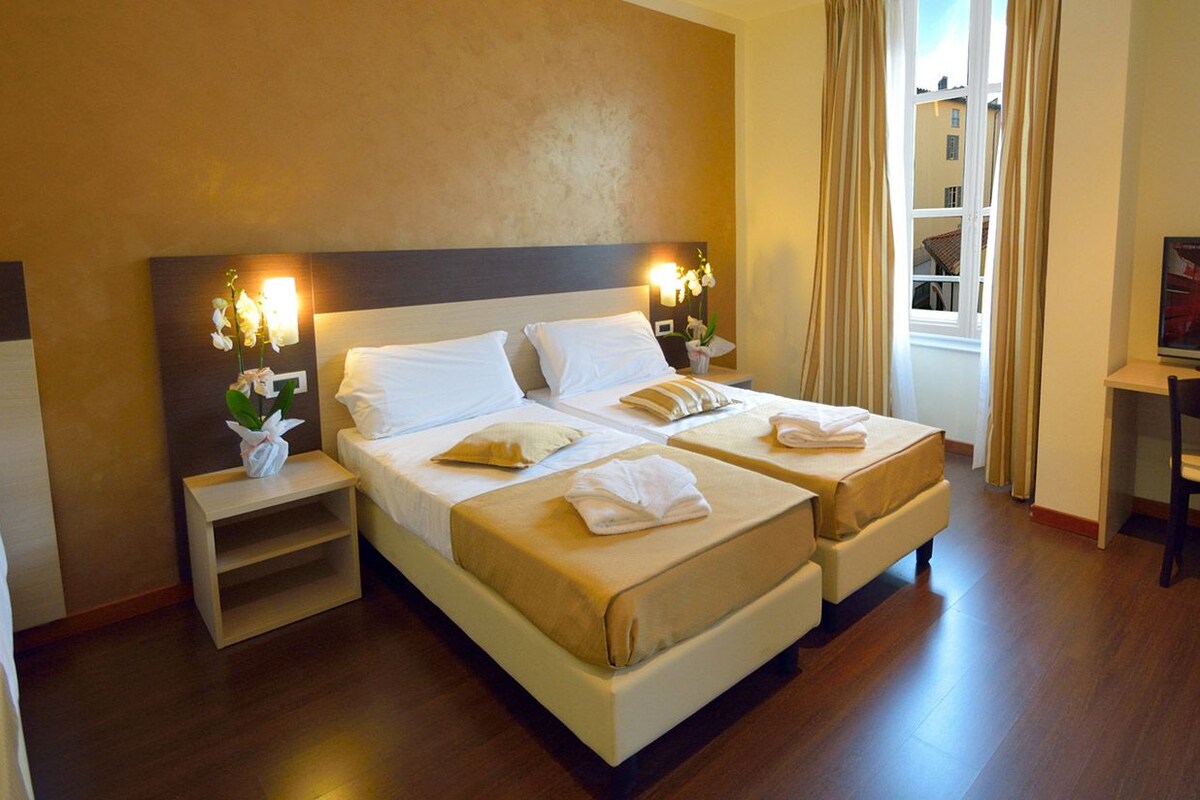 A hotel room with two beds, a TV, a desk, and a window with curtains.