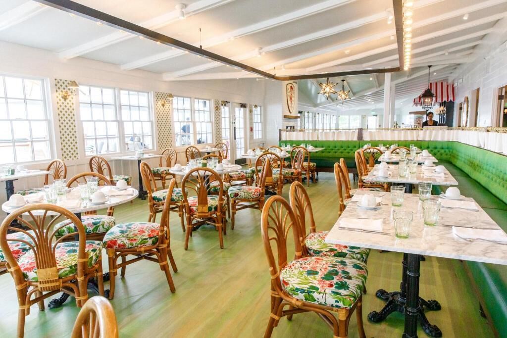 A restaurant with round tables, wooden chairs, and a green booth area.