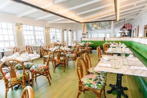 A restaurant with round tables, wooden chairs, and a green booth area. - The Pridwin Hotel (Shelter Island Heights)