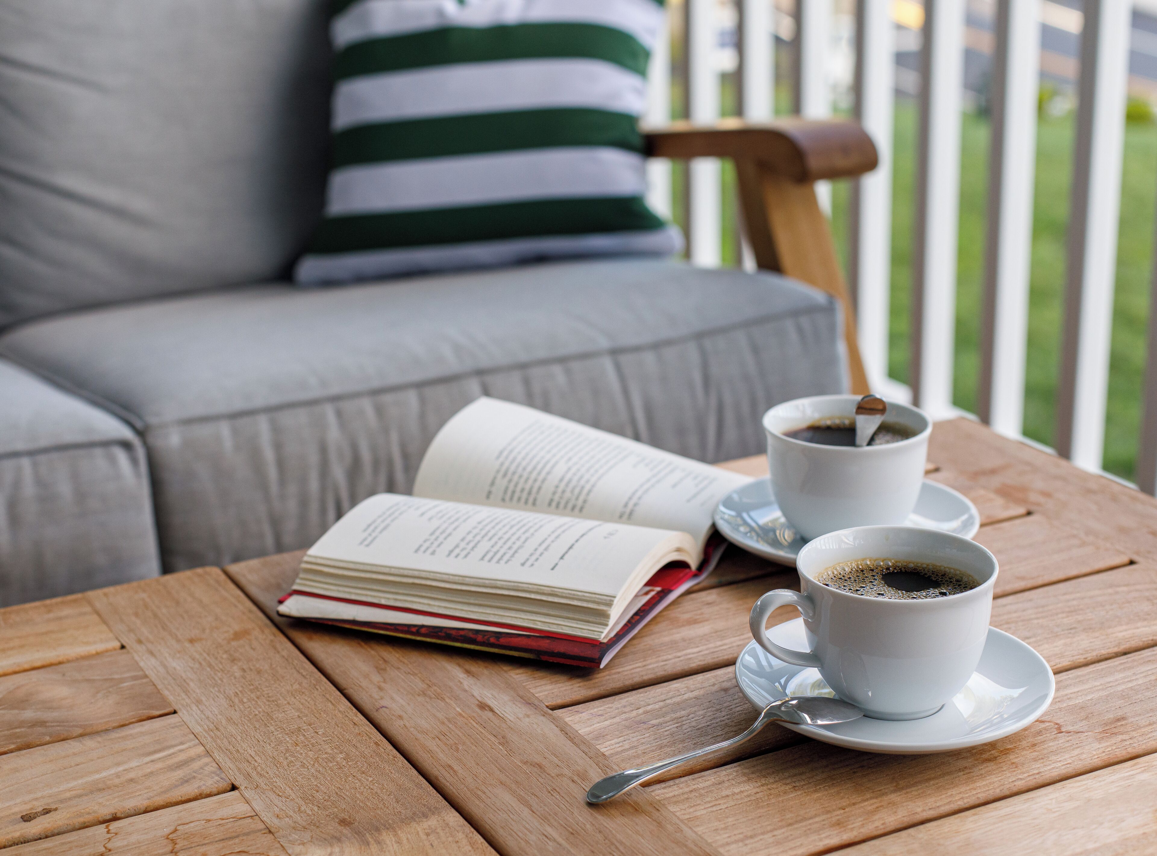 A wooden table with a book, two cups of coffee, and a spoon.