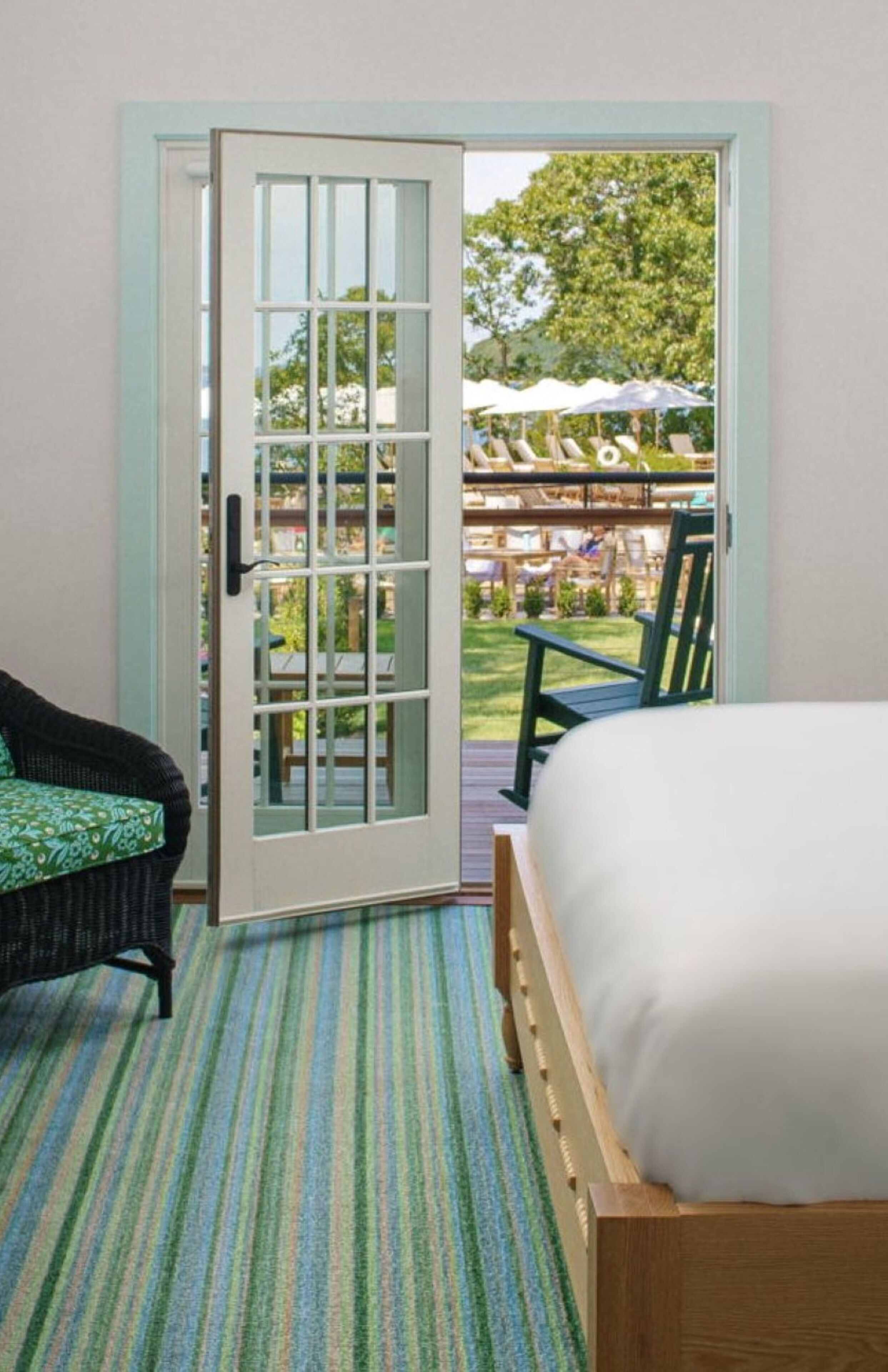 Un dormitorio con cama, una silla y una puerta que da a un espacio exterior con terraza y sombrillas.