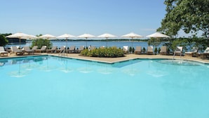 En pool med solstolar och parasoller, omgiven av grönska och med utsikt över havet.