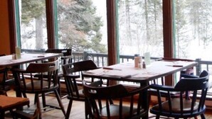 A restaurant with multiple tables and chairs, large windows with a view of trees, and a wooden interior. - Amizette Inn and Restaurant (Taos Ski Valley)