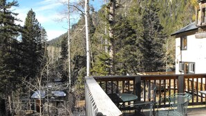 A wooden deck with outdoor furniture, surrounded by a forested area and a mountain backdrop. - Amizette Inn and Restaurant (Taos Ski Valley)