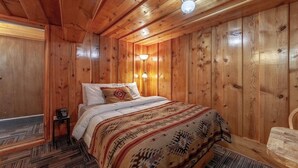 A wooden-paneled room with a bed, a telephone, and a wall-mounted light fixture. - Amizette Inn and Restaurant (Taos Ski Valley)
