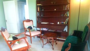 A room with a wooden bookshelf, two chairs, and a small table. - The Teacherage (Sunbury)