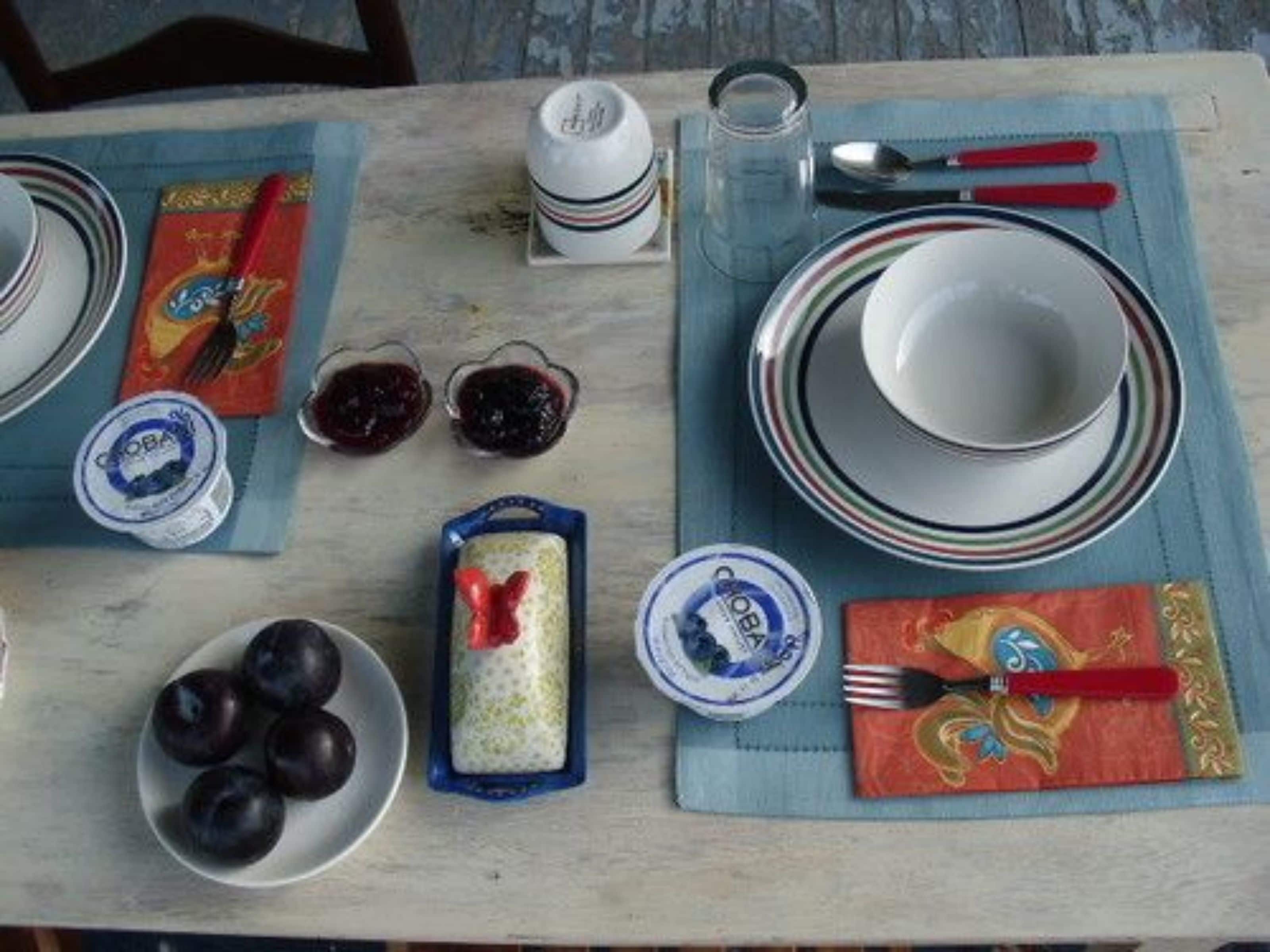 A table set with plates, bowls, and cutlery, with a napkin and a small container of jam.