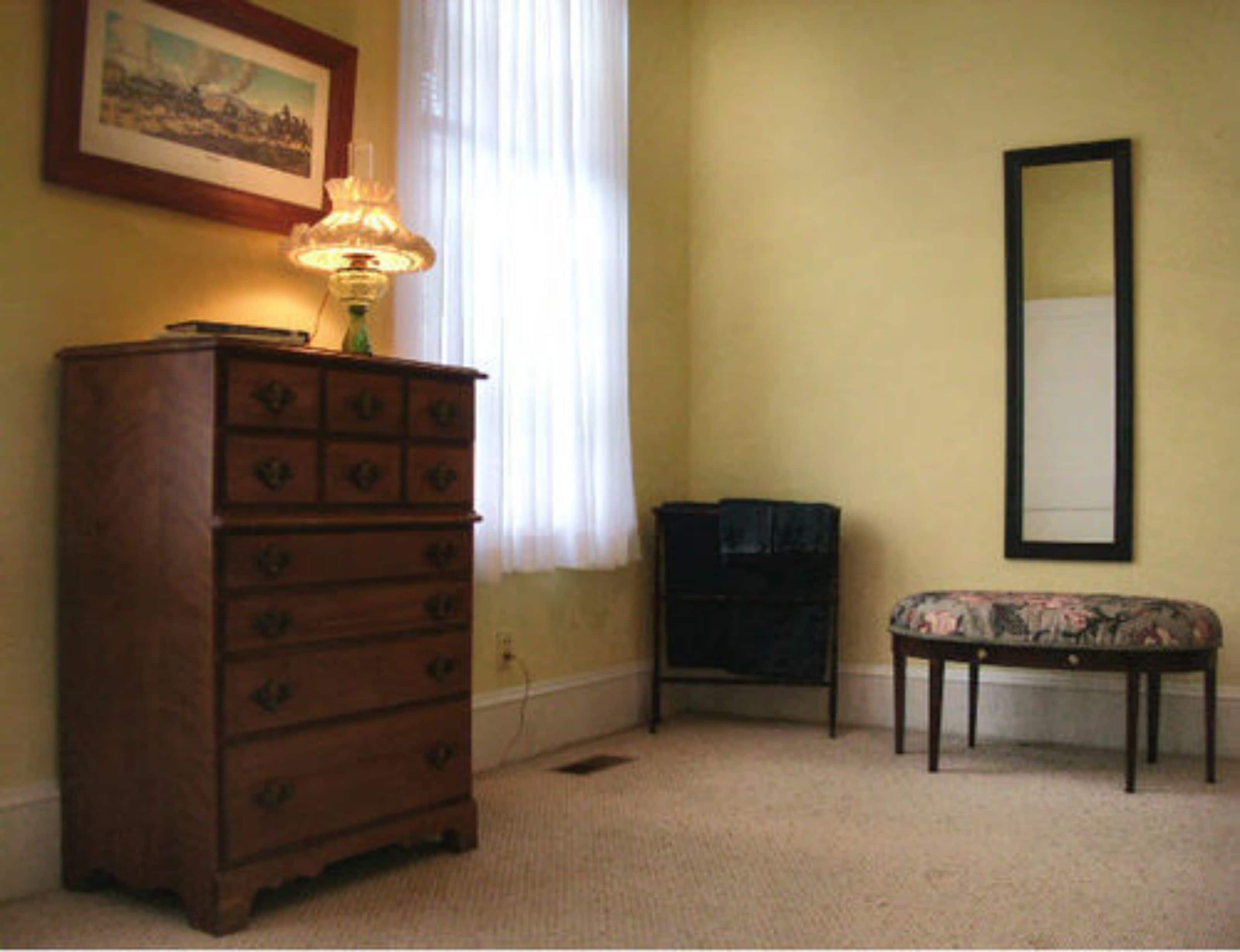 A room with a wooden dresser, a bench, a mirror, and a lamp.