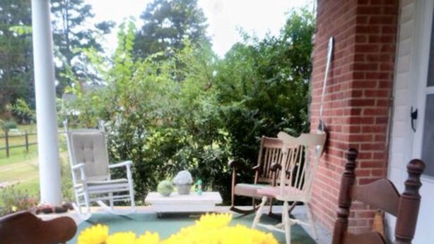 A porch with two rocking chairs and a small table, surrounded by yellow flowers. - The Teacherage (Sunbury)