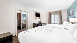 A hotel room with two beds, a desk, a TV, and a door leading to a bathroom.