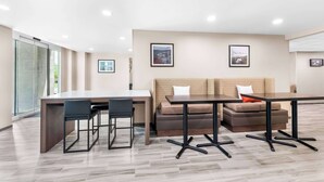 A modern hotel room with a dining area, a sofa, and a large window.