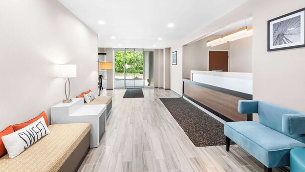 A modern hotel lobby with a reception desk, seating area, and a view of the outdoors.
