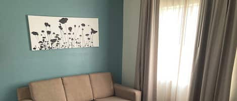 Ett vardagsrum med en beige soffa, ett svart soffbord och ett väggmonterat konstverk som föreställer blommor.
