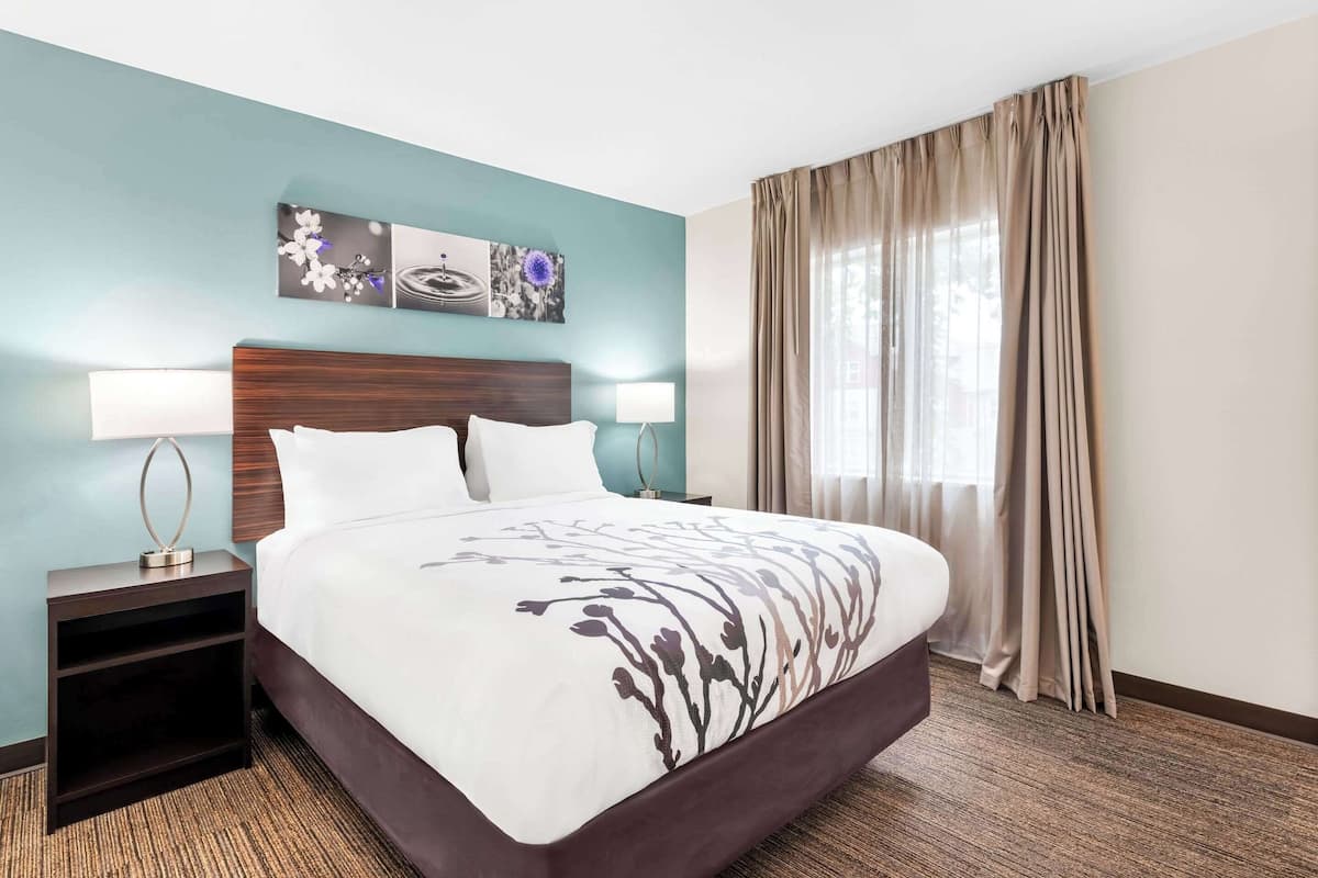 Habitación de hotel con una cama grande, dos mesitas de noche con lámparas, un cabecero y una ventana con cortinas.