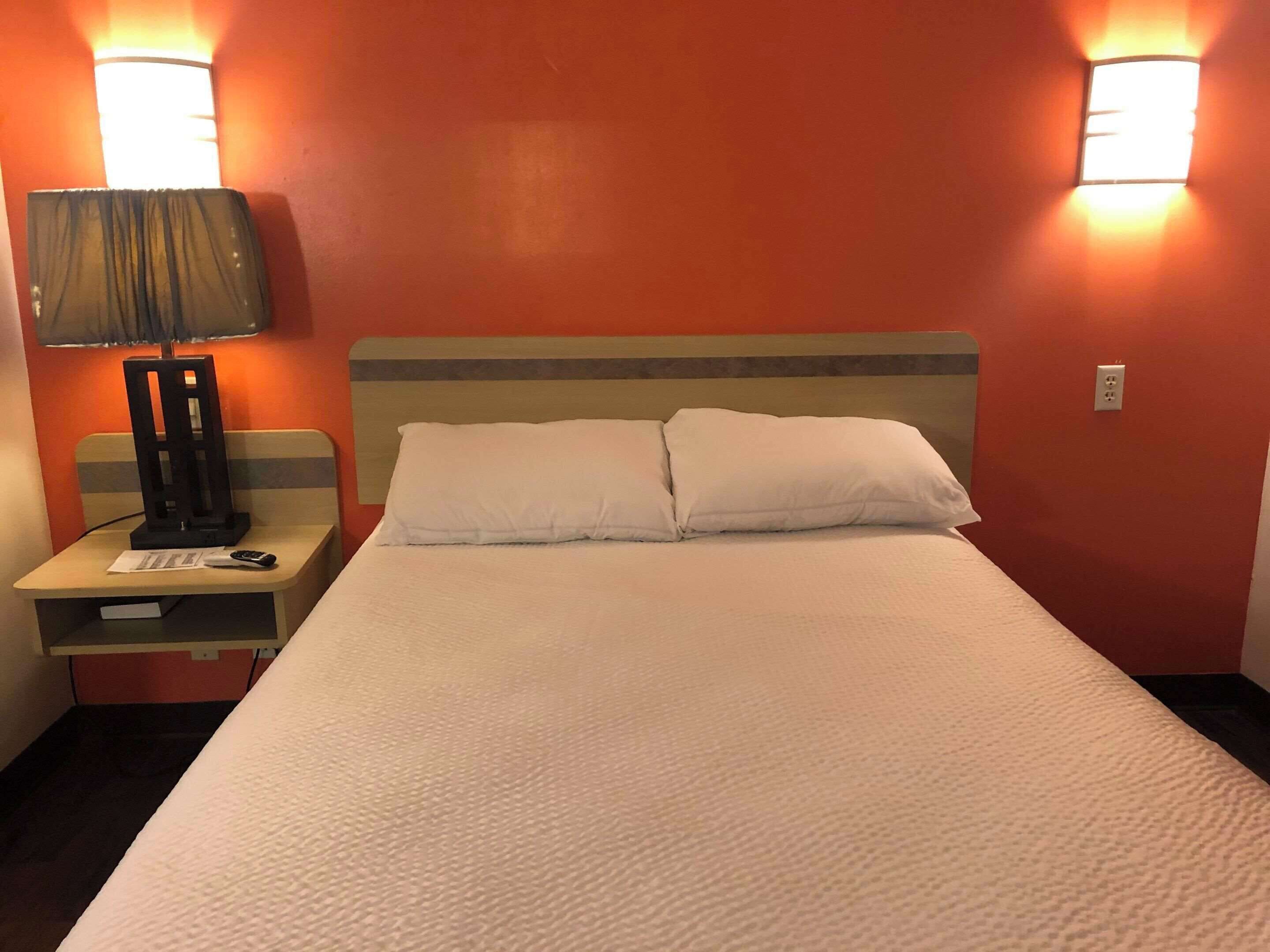 A hotel room with a bed, a nightstand, a lamp, and two wall-mounted lights.