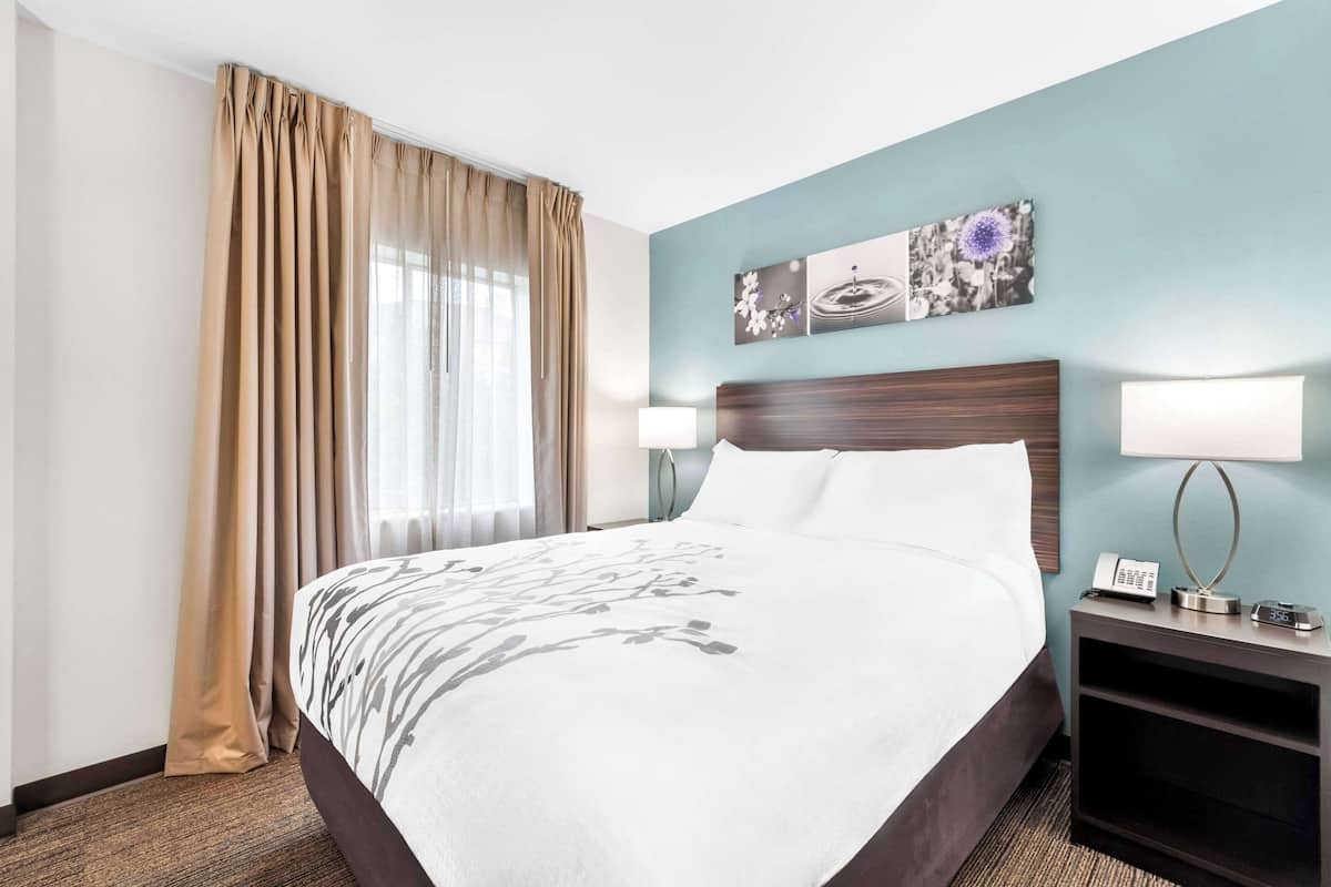 Una habitación de hotel con una cama grande, dos lámparas de noche, una mesita de noche con un teléfono y una ventana con cortinas.