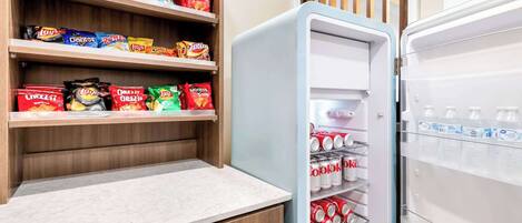 Eine Küche mit Holzböden und Regalen voller Snacks sowie ein Kühlschrank mit Limodosen.