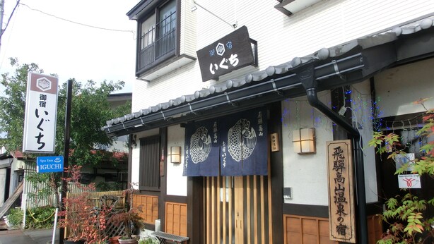 A traditional Japanese building with a wooden entrance, a signboard with Japanese characters, and a small outdoor seating area with a bench. - Spa Inn Oyado Iguchi (Takayama)