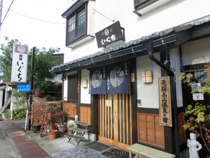 A traditional Japanese building with a wooden entrance, a signboard with Japanese characters, and a small outdoor seating area with a bench. - Spa Inn Oyado Iguchi (Takayama)