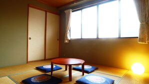 A tatami mat room with a low table and cushions, a sliding door, and a window with curtains. - Spa Inn Oyado Iguchi (Takayama)