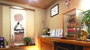 A traditional Japanese room with tatami flooring, a wooden bench, a shelf with shoes, a mirror, and a wall with calligraphy and a framed picture. - Spa Inn Oyado Iguchi (Takayama)
