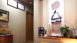 A traditional Japanese room with tatami flooring, a shoji screen door, a wooden bench, and a shelf with various items including a plant and a framed picture. - Spa Inn Oyado Iguchi (Takayama)