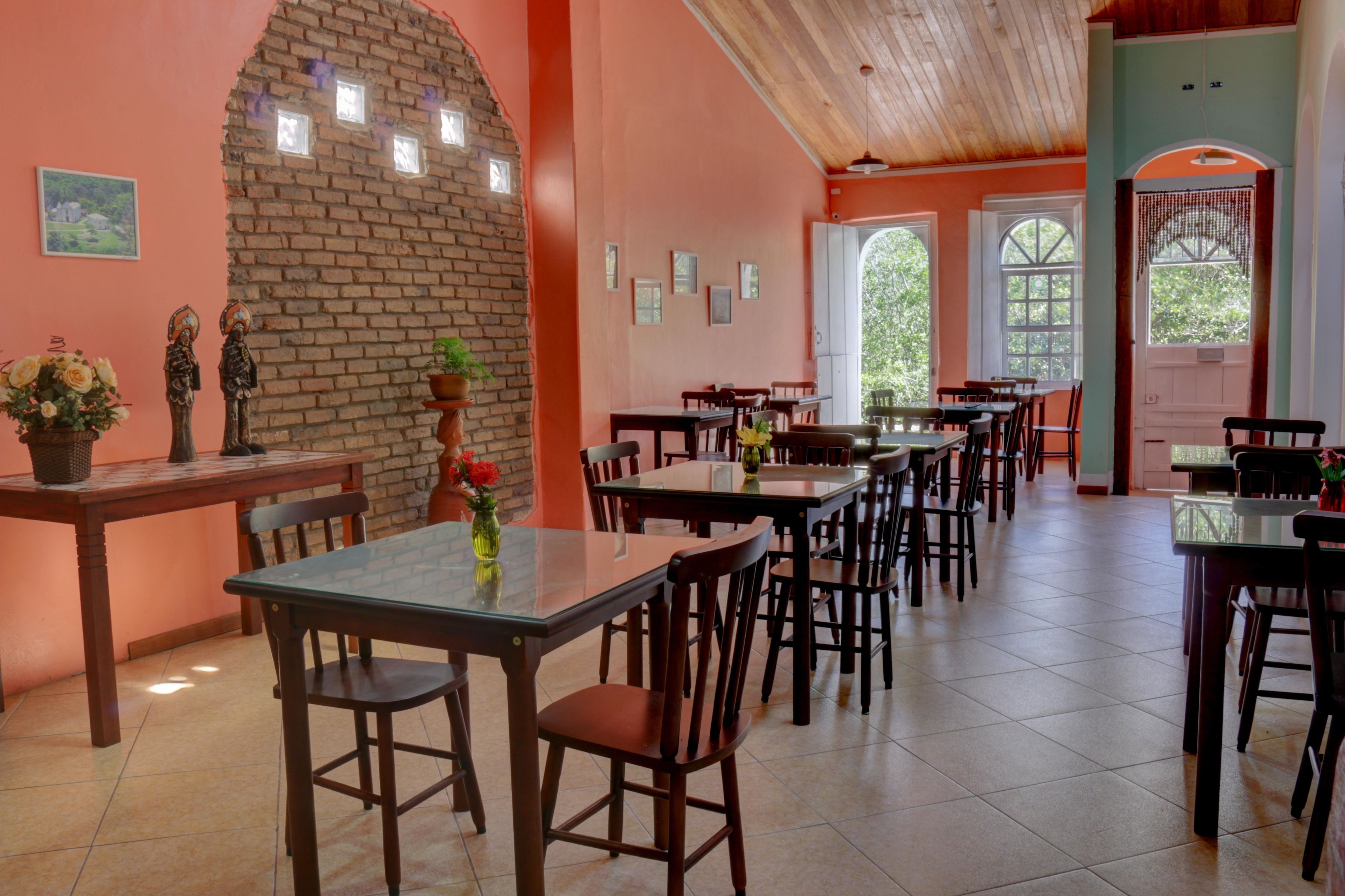 Un espace repas avec des murs en briques, des tables et des chaises en bois. Des plantes en pot et des tableaux encadrés décorent les murs.