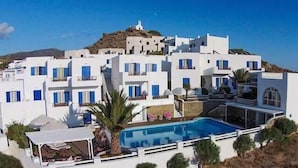 Un edificio blanco con piscina y una colina al fondo.