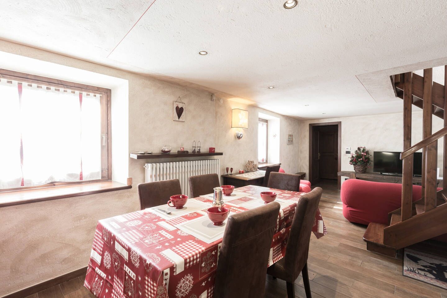 Un comedor con una mesa dispuesta para cuatro personas, un sofá rojo y una escalera que lleva a otro nivel.