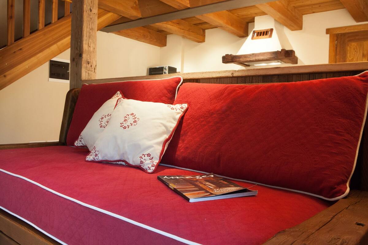 A cozy room with a wooden staircase, a red sofa with a white pillow, and a book on the sofa.