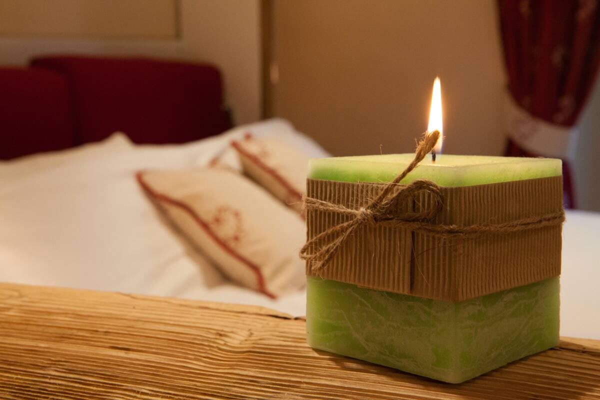A lit candle on a square green soap bar tied with twine, placed on a wooden surface.