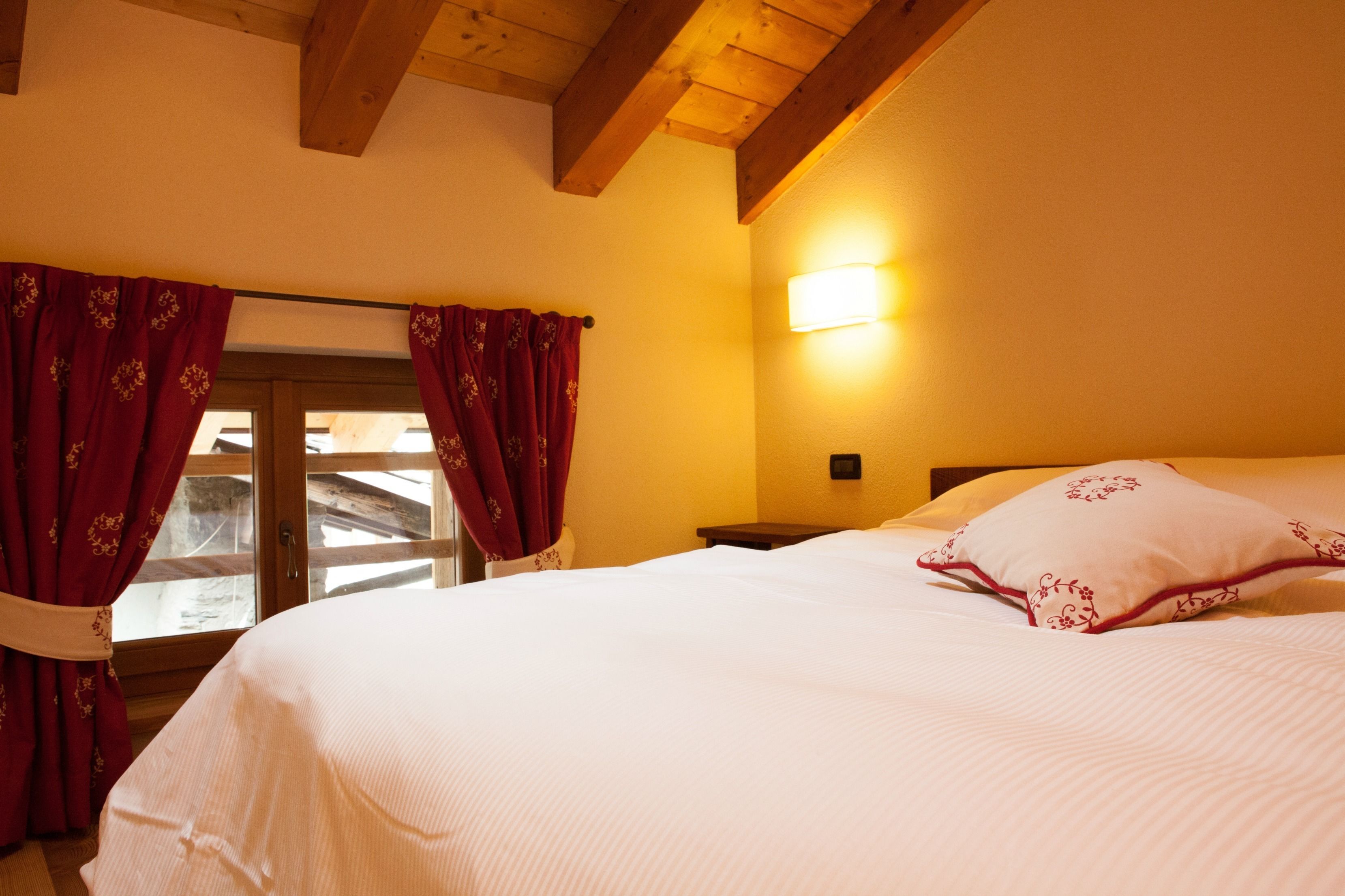 Une chambre à coucher avec un lit, des rideaux rouges, une table de chevet et une lampe fixée au mur.